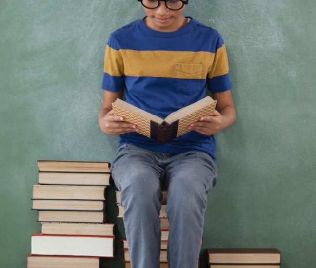 Schoolboy sitting on books stack and reading book Schoolboy sitting on books stack and reading book